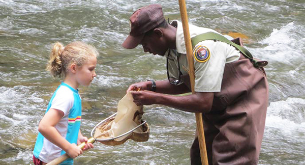 A high school intern helps a young girl during a Stream Splashers Junior Ranger program