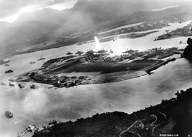 Photograph taken from a Japanese plane during the torpedo attack on ships moored on both sides of Ford Island shortly after the beginning of the Pearl Harbor attack. View looks about east, with the supply depot, submarine base and fuel tank farm in the right center distance. A torpedo has just hit USS West Virginia on the far side of Ford Island (center). Other battleships moored nearby are (from left): Nevada, Arizona, Tennessee (inboard of West Virginia), Oklahoma (torpedoed and listing) alongside Maryland, and California. On the near side of Ford Island, to the left, are light cruisers Detroit and Raleigh, target and training ship Utah and seaplane tender Tangier. Raleigh and Utah have been torpedoed, and Utah is listing sharply to port. Japanese planes are visible in the right center (over Ford Island) and over the Navy Yard at right. U.S. Navy planes on the seaplane ramp are on fire. Japanese writing in the lower right states that the photograph was reproduced by authorization of the Navy Ministry.